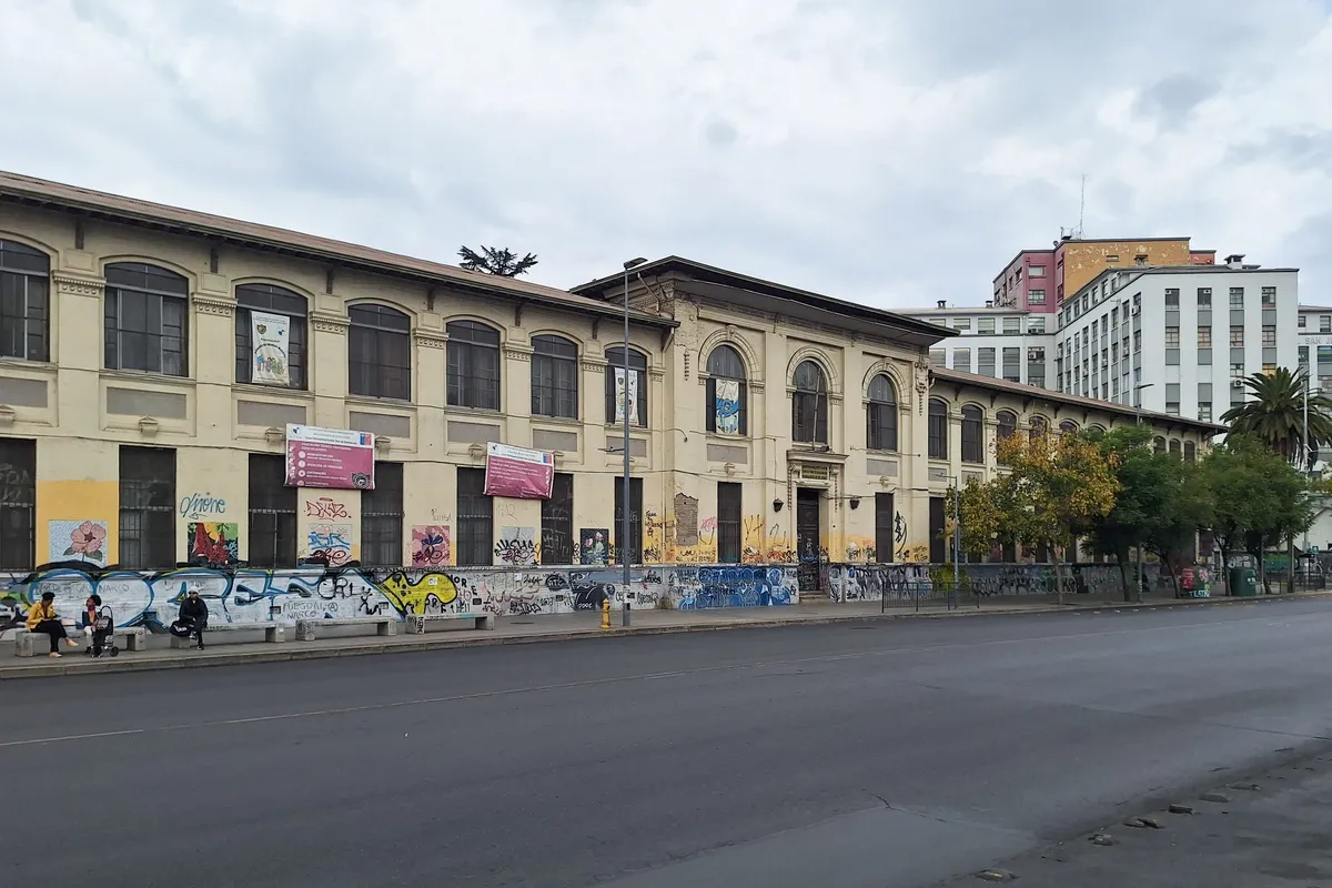 Fachada larga y amarilla del liceo Emilia Toro de Balmaceda, frente a una avenida del Barrio Balmaceda.