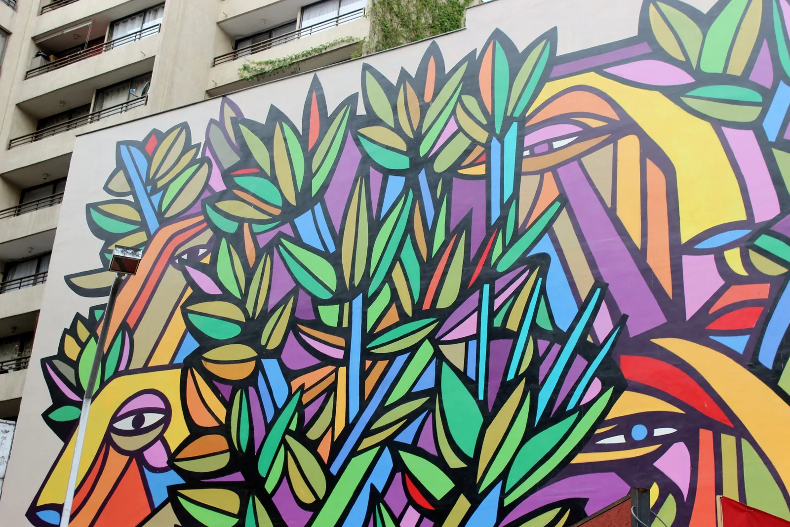 Mural de gran formato con figuras y hojas de colores pintado en la medianera de un edificio, junto al metro Bellas Artes.