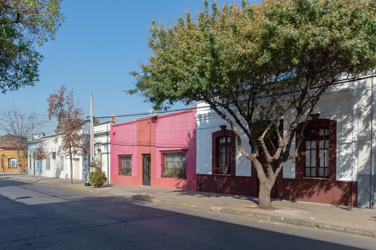 Casas continuas de un piso pintadas de rosado y blanco en la calle Lira, Barrio Matta Sur, con un árbol en la vereda.